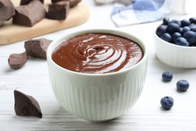 Photo of Delicious chocolate cream and blueberries on white wooden table, closeup