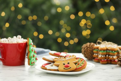 Photo of Decorated cookies and hot drink on white marble table against blurred Christmas lights