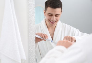 Man squeezing toothpaste from tube onto electric toothbrush in bathroom