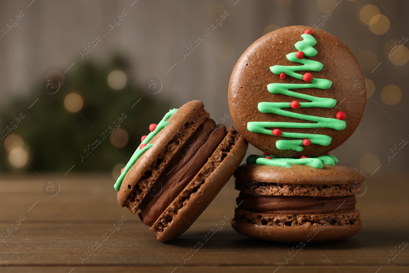 Photo of Beautifully decorated Christmas macarons on wooden table against blurred festive lights