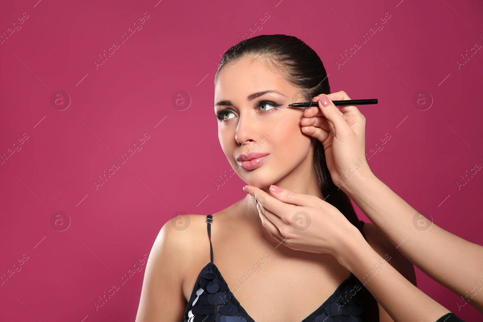 Photo of Artist applying makeup onto woman's face on pink background, space for text