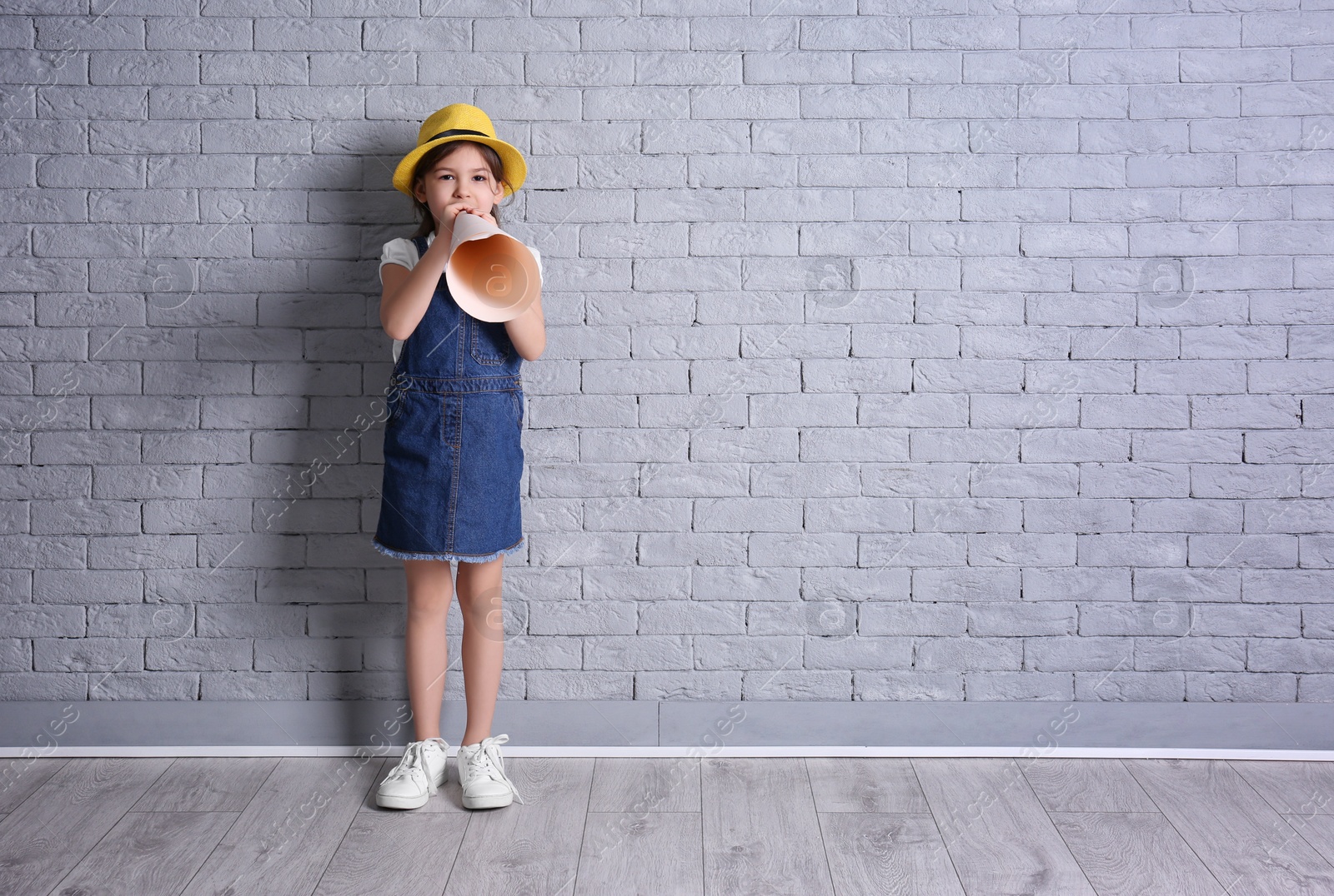 Photo of Adorable little girl with paper megaphone on brick wall background