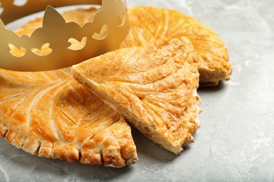 Photo of Traditional galette des Rois with paper crown on light grey marble table, closeup