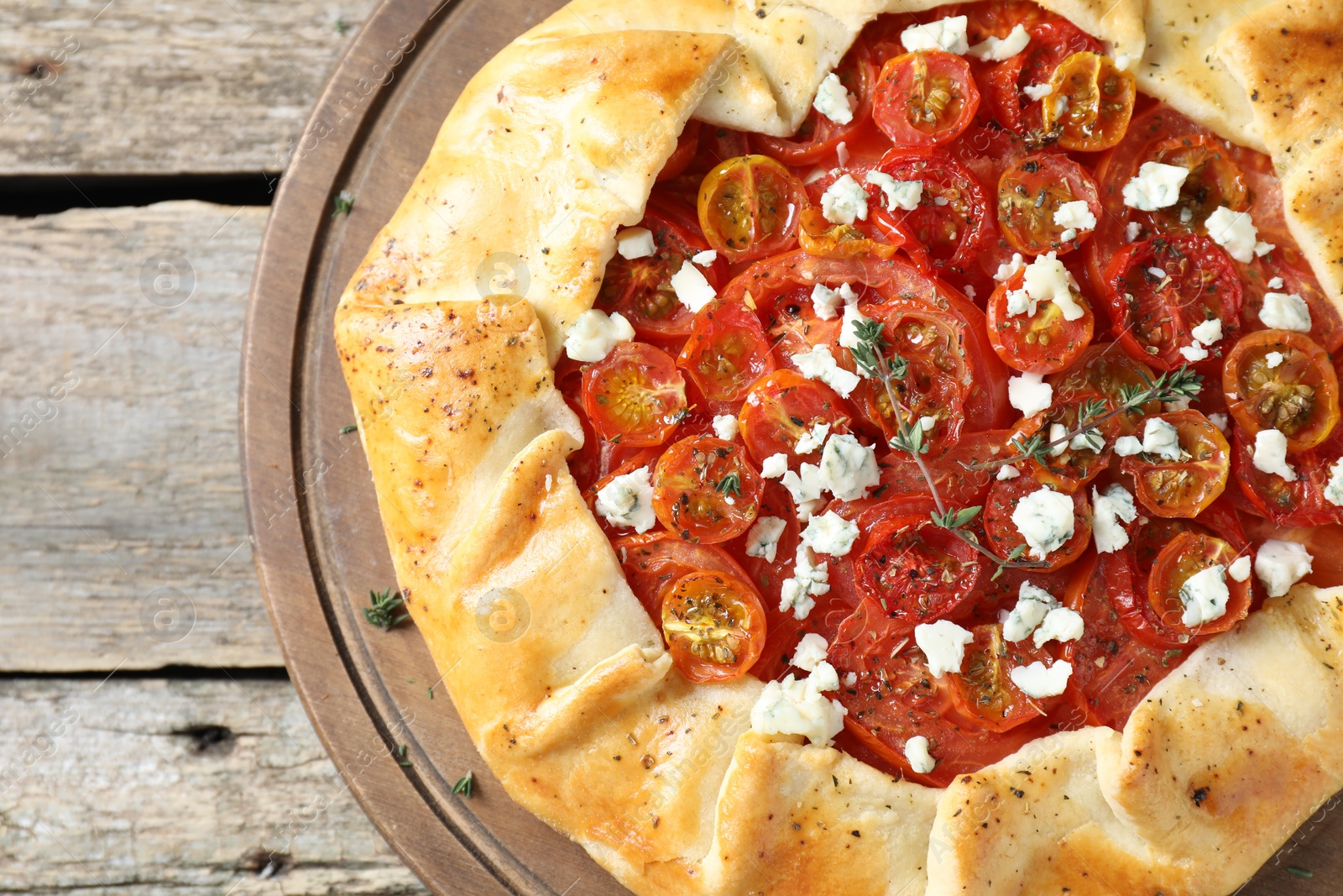 Photo of Tasty galette with tomato, thyme and cheese (Caprese galette) on wooden table, top view. Space for text