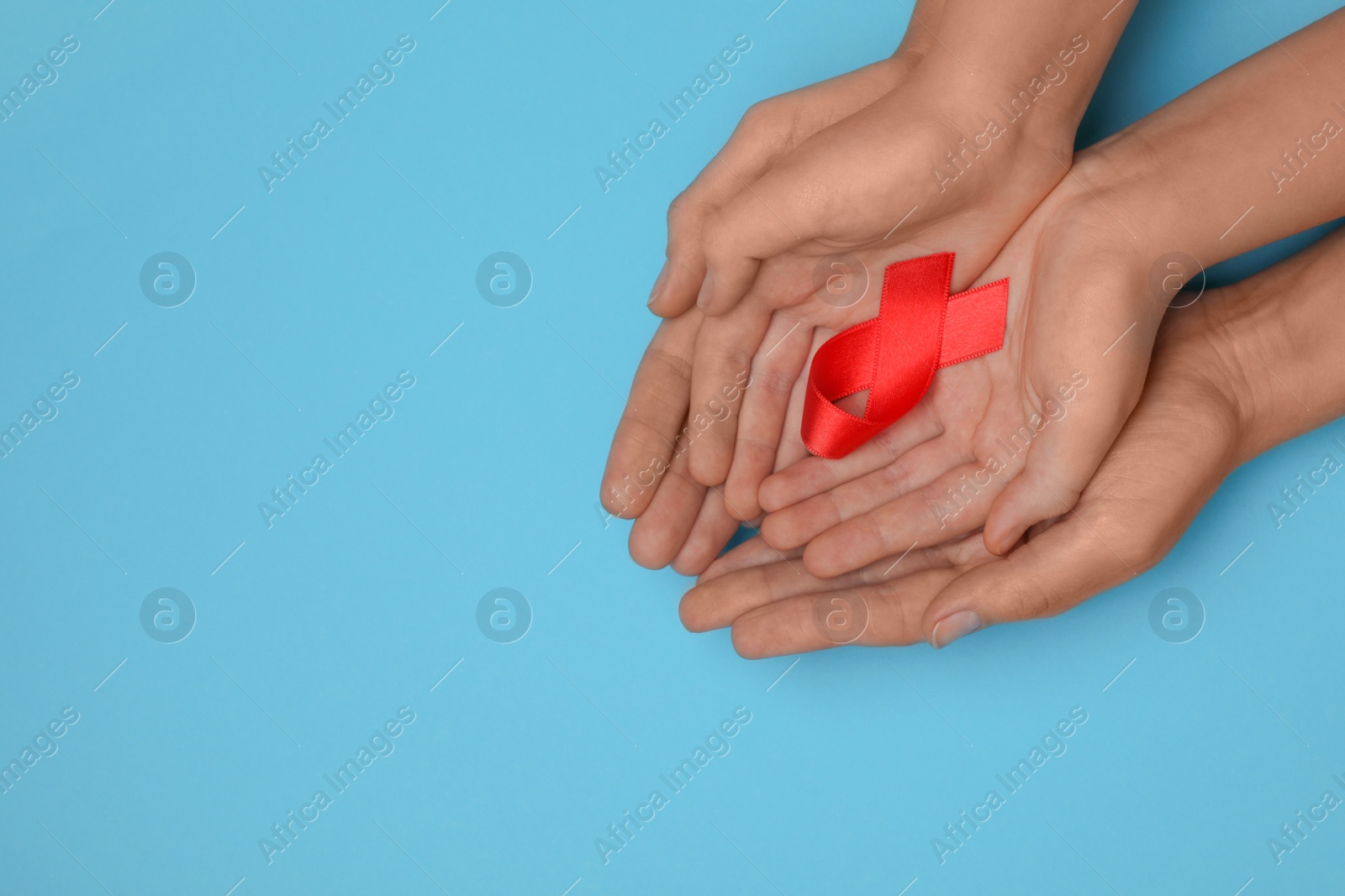 Photo of Woman and girl holding red ribbon on blue background, top view with space for text. AIDS disease awareness