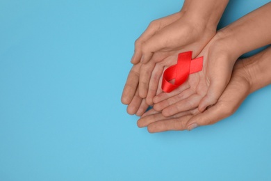 Photo of Woman and girl holding red ribbon on blue background, top view with space for text. AIDS disease awareness