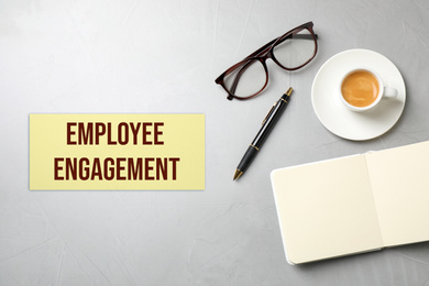 Cup of coffee, glasses and text EMPLOYEE ENGAGEMENT on grey background, flat lay