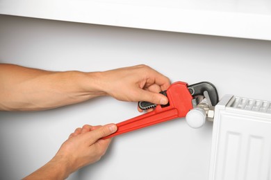 Professional plumber using adjustable wrench for installing new heating radiator, closeup