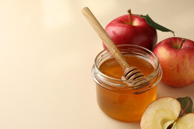 Photo of Delicious apples, jar of honey and dipper on beige background, closeup. Space for text