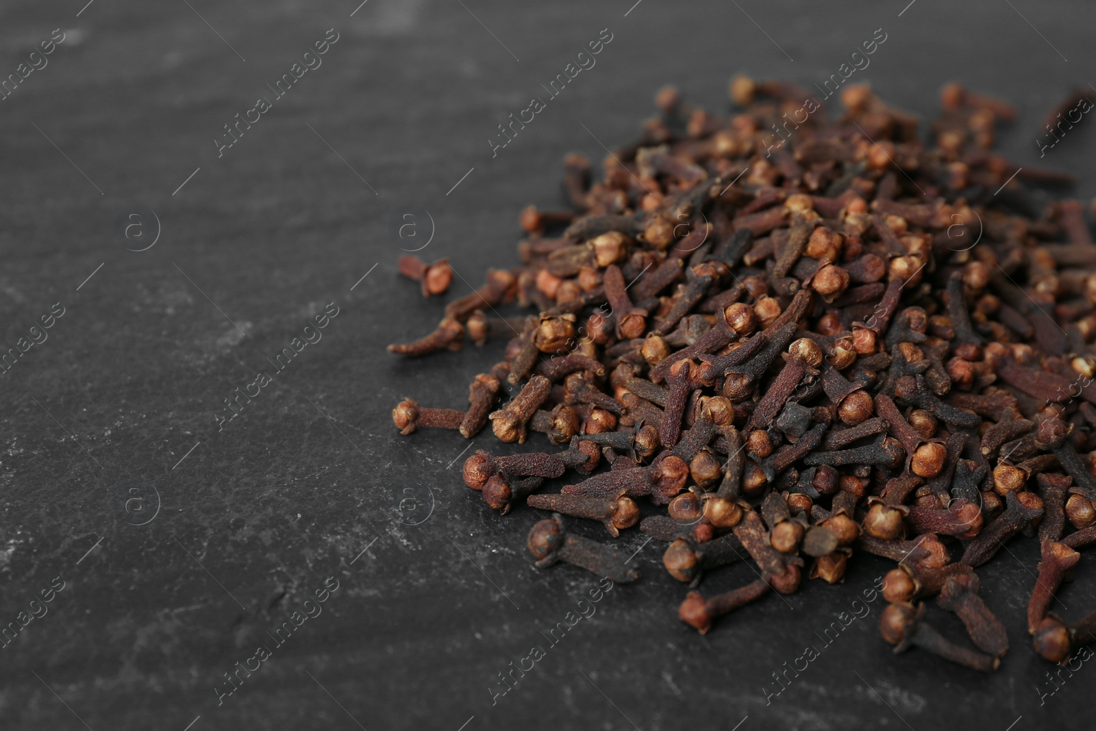 Photo of Pile of aromatic dry cloves on black table, closeup. Space for text