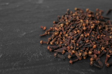 Photo of Pile of aromatic dry cloves on black table, closeup. Space for text