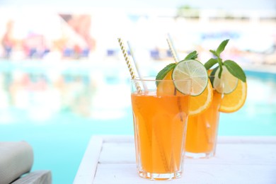 Photo of Refreshing cocktail in glasses near outdoor swimming pool on sunny day. Space for text