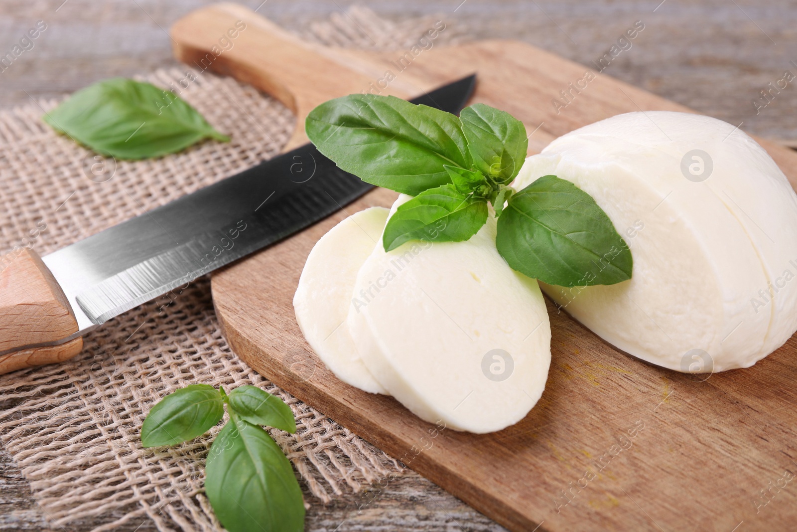 Photo of Slices of tasty mozzarella, basil leaves and knife on wooden table, closeup