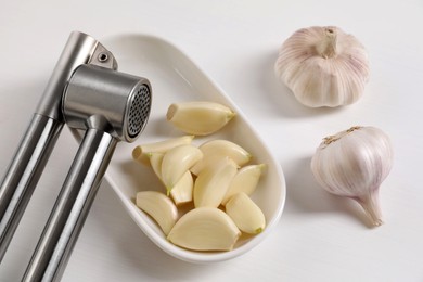 Metal press and garlic on white wooden table, flat lay