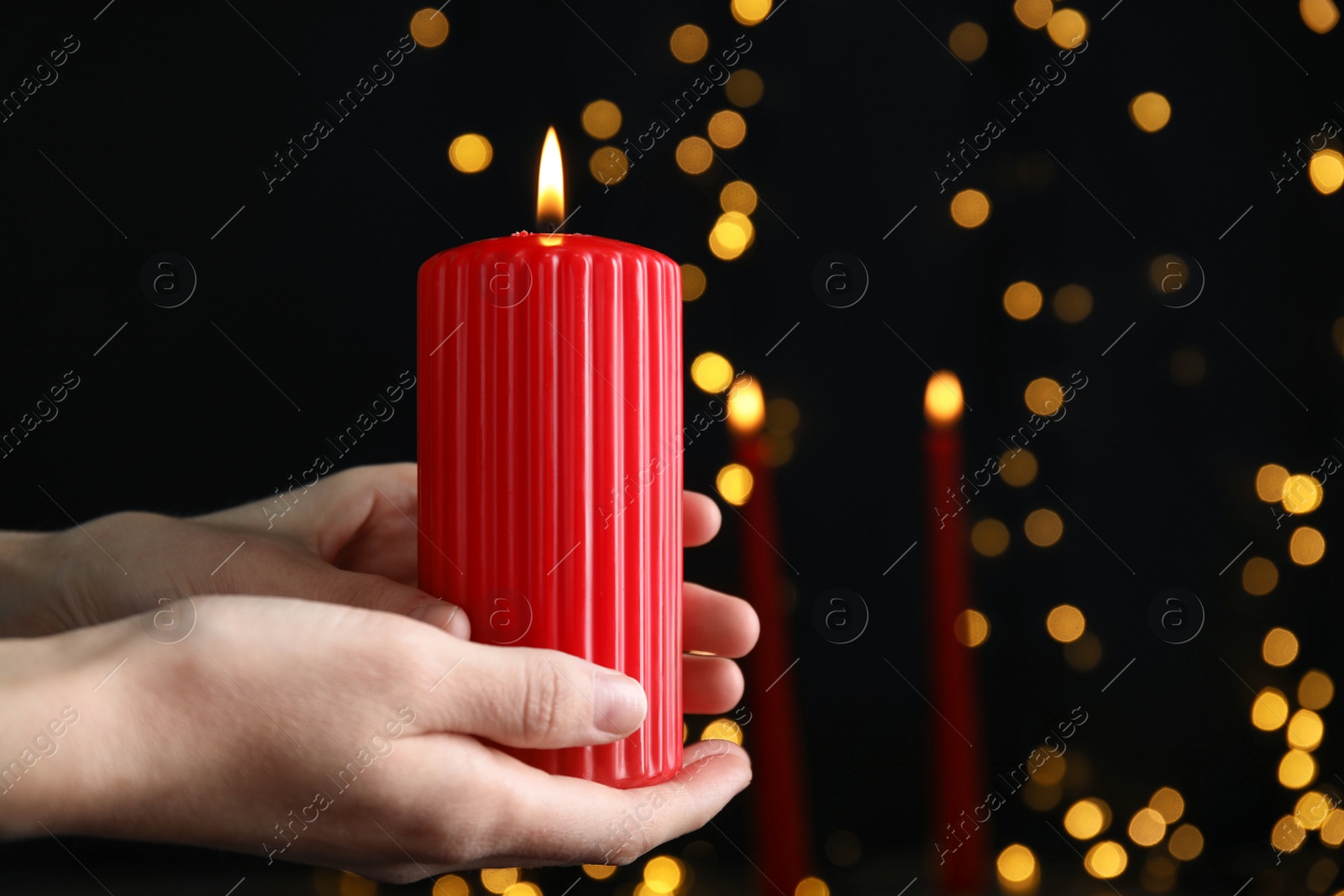 Photo of Woman holding burning red candle against blurred Christmas lights, closeup. Space for text