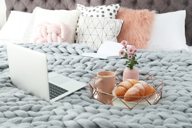 Tray with tasty breakfast, laptop and book on bed