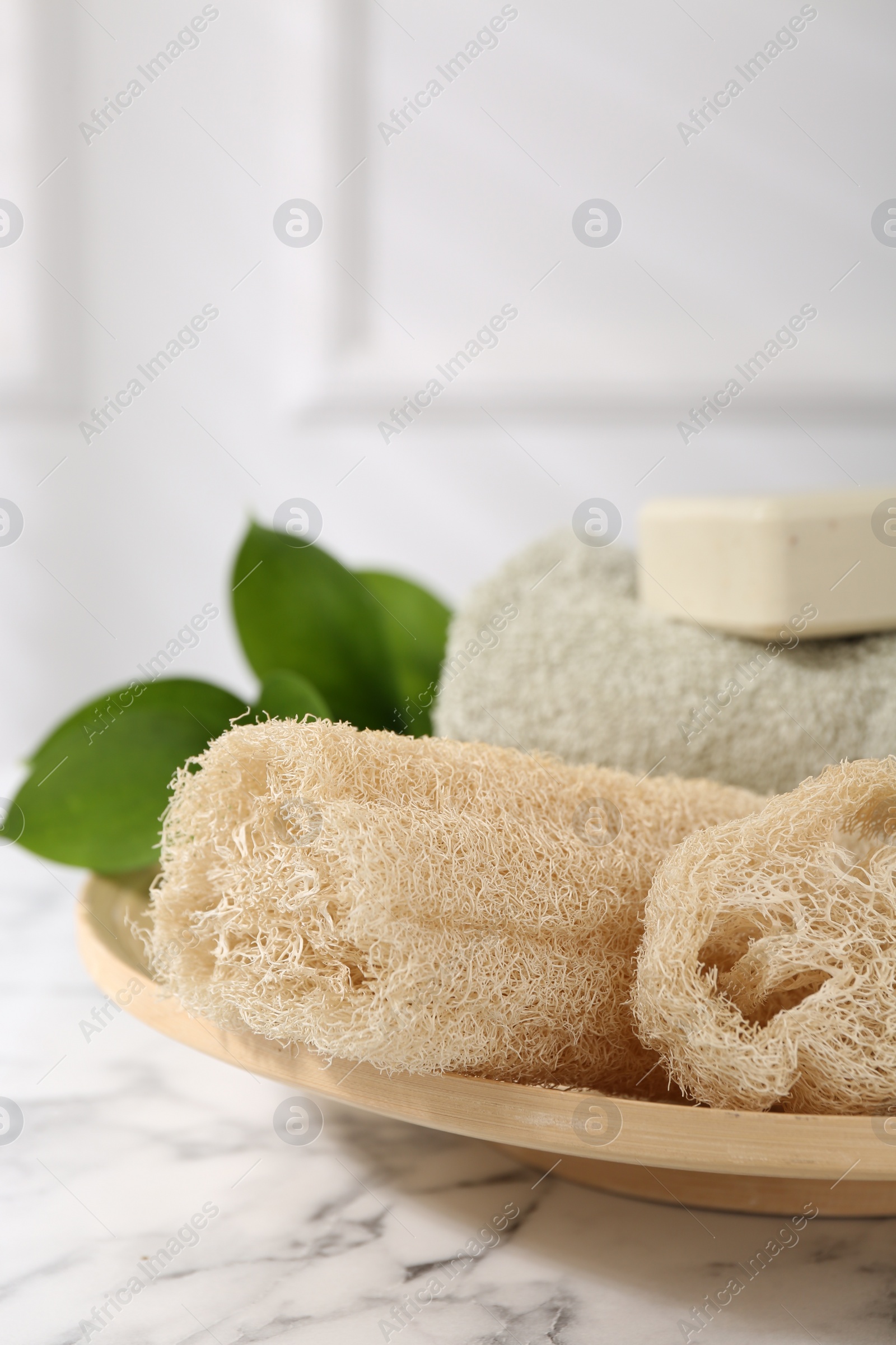 Photo of Loofah sponges, soap, towel and green leaves on white marble table