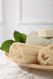 Loofah sponges, soap, towel and green leaves on white marble table