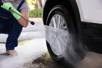 Photo of Worker washing auto with high pressure water jet at outdoor car wash, closeup