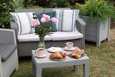 Photo of Morning drink, pastry, berries, cheese and vase with flowers on rattan table. Summer breakfast outdoors