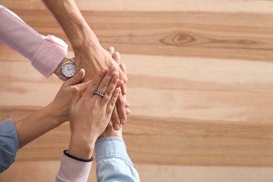 Photo of People holding hands together over wooden background, top view with space for text. Unity concept