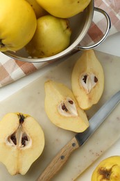 Photo of Tasty ripe quinces, metal colander and knife on white wooden table, flat lay