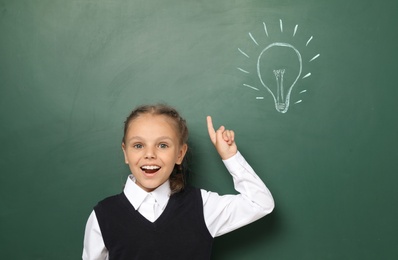 Photo of Little school child in uniform near chalkboard with lightbulb drawing