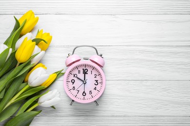 Photo of Pink alarm clock and beautiful tulips on white wooden table, flat lay with space for text. Spring time