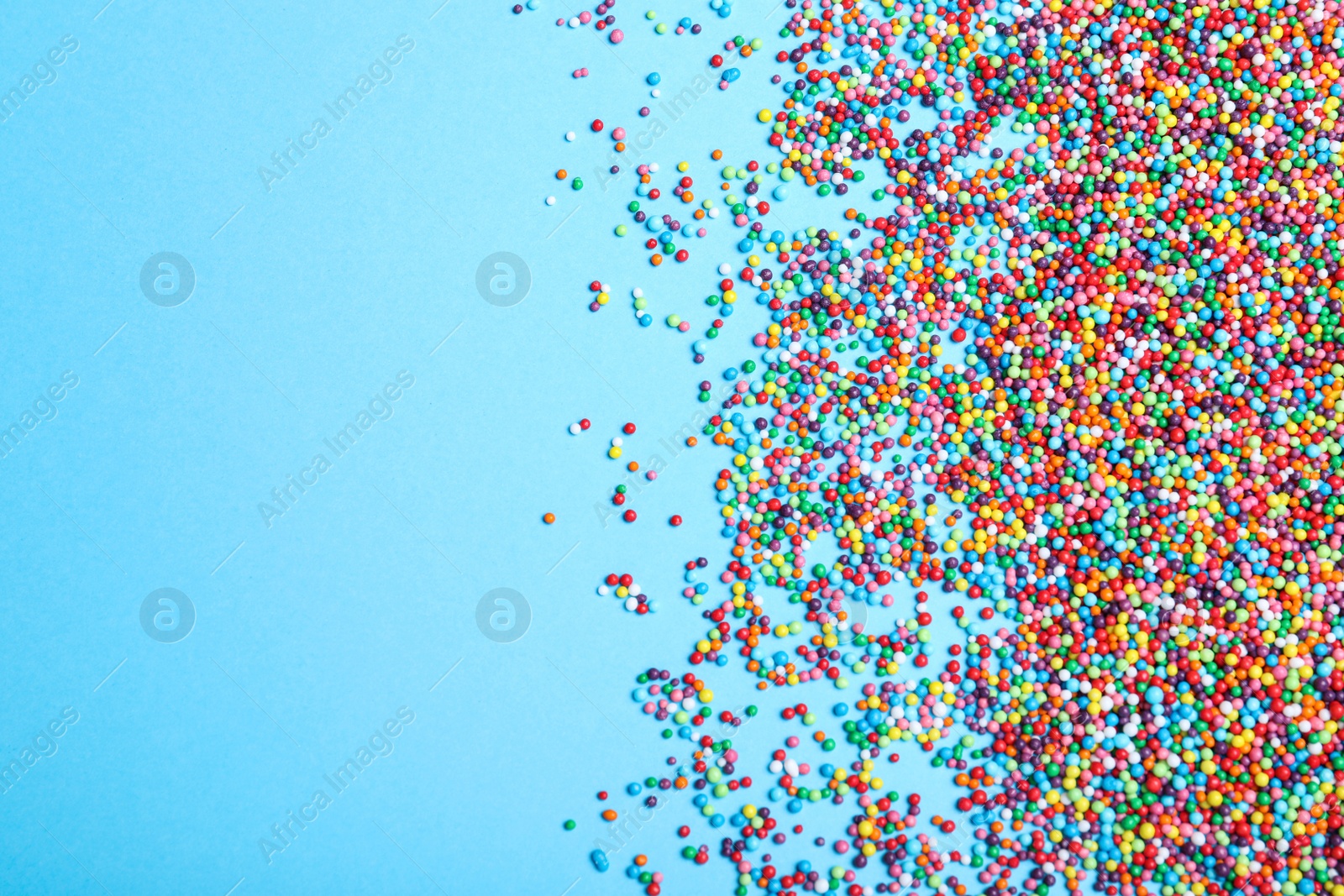 Photo of Colorful sprinkles on light blue background, flat lay with space for text. Confectionery decor