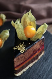 Photo of Piece of tasty cake decorated with physalis fruit on slate plate, closeup
