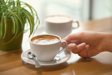 Woman with cup of aromatic coffee at wooden table