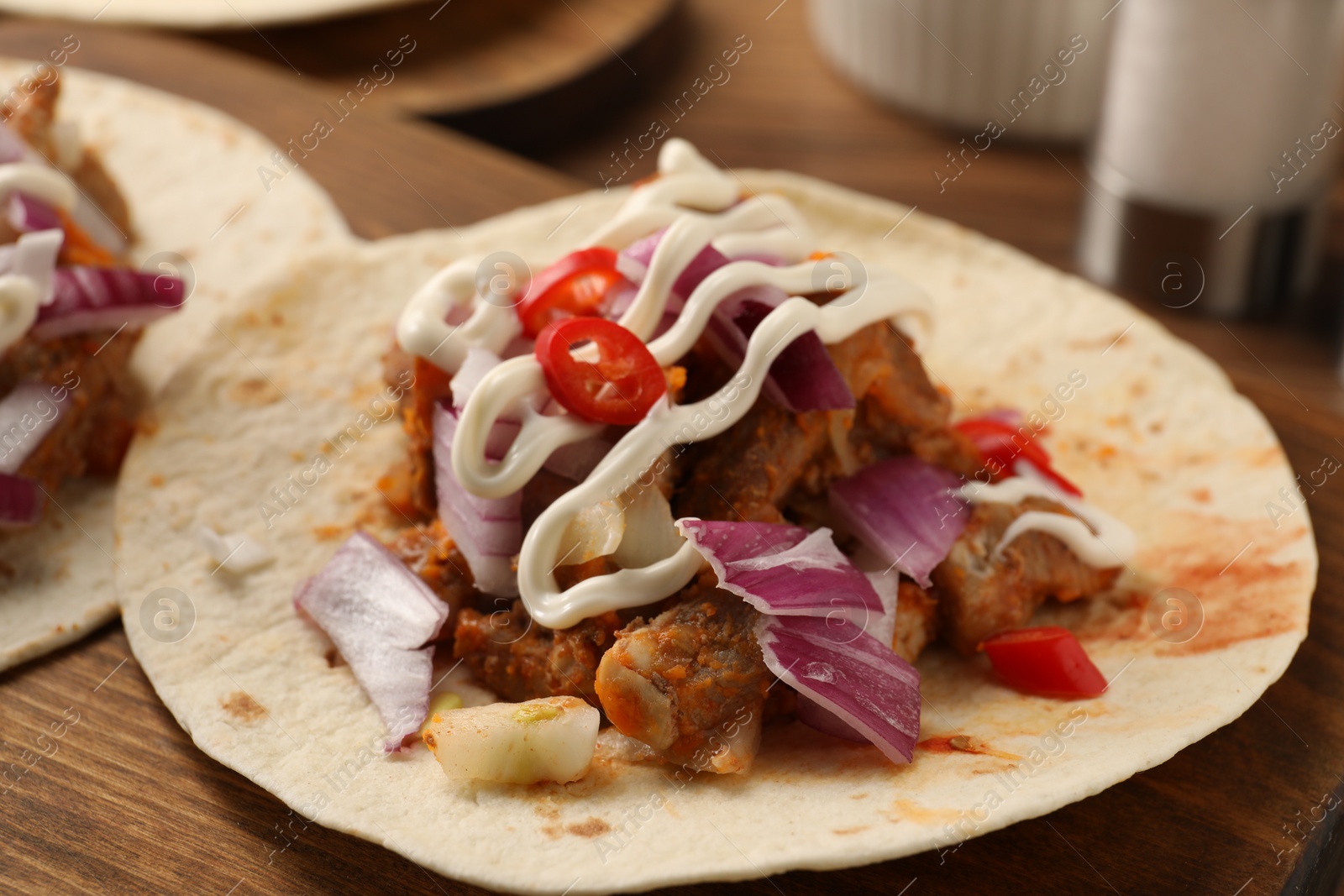 Photo of Delicious tacos with vegetables, meat and sauce on wooden table, closeup