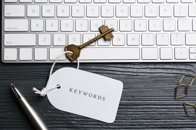 Photo of Key with tag KEYWORD and computer keyboard on black wooden table, flat lay