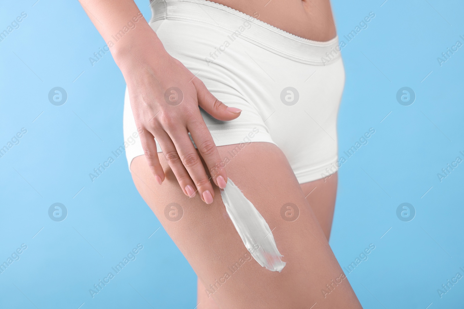 Photo of Woman with smear of body cream on her leg against light blue background, closeup