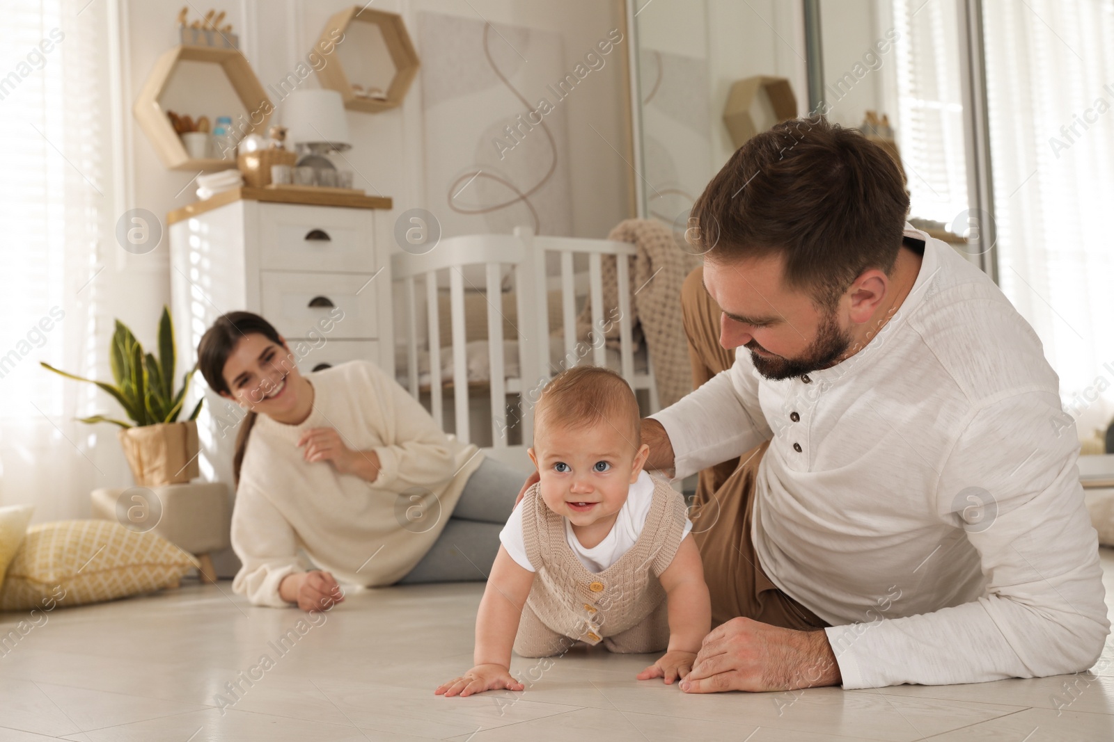 Photo of Happy parents helping their baby to crawl on floor at home