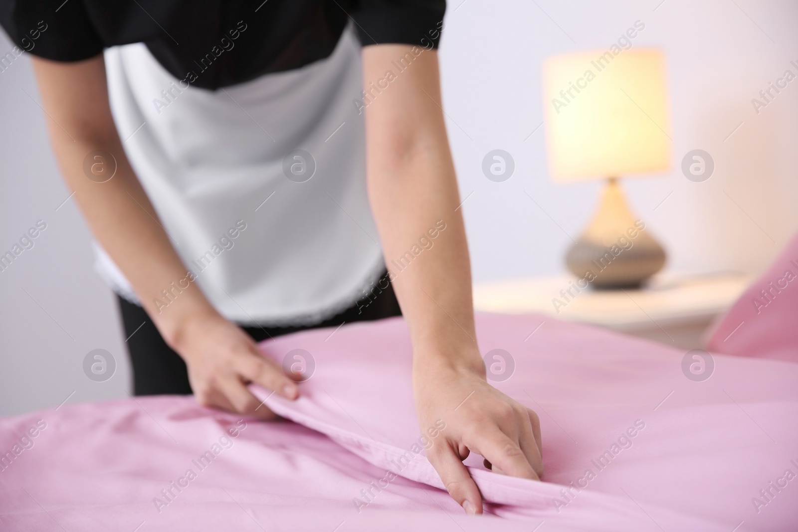 Photo of Young maid making bed in hotel room