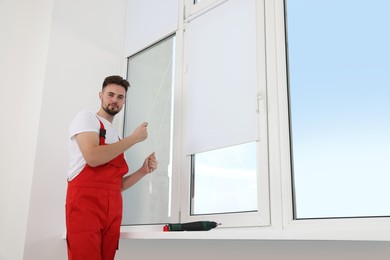 Worker in uniform opening roller window blind indoors
