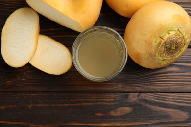 Photo of Glass of fresh natural turnip juice, cut and whole roots on wooden table, flat lay