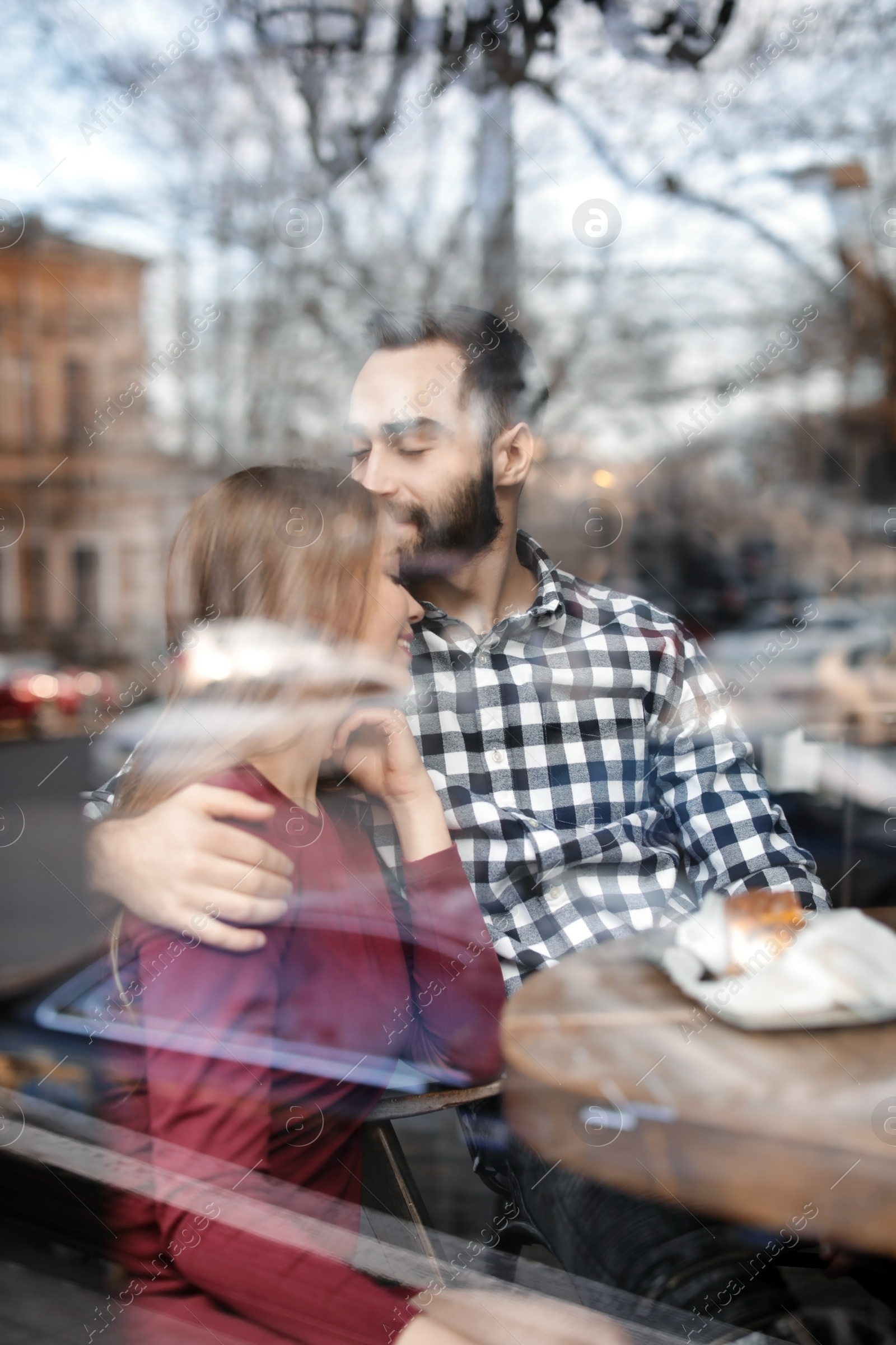 Photo of Lovely young couple spending time together in cafe, view from outdoors through window