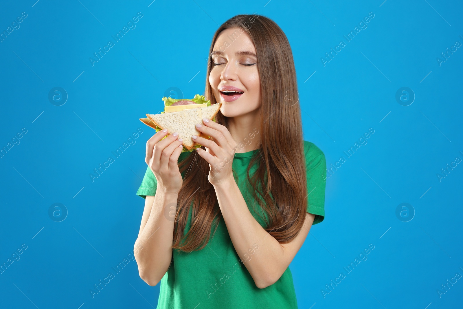 Photo of Young woman eating tasty sandwich on light blue background