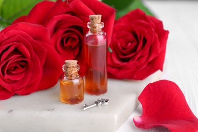 Photo of Bottles of love potion, red rose flowers and small key on table, closeup