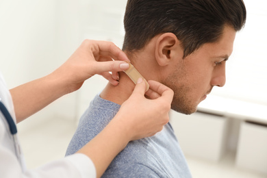 Photo of Doctor putting sticking plaster onto man's neck indoors