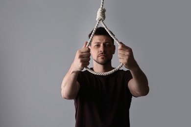 Depressed man with rope noose on light grey background