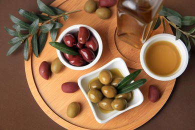 Oil, olives and tree twigs on brown table, top view