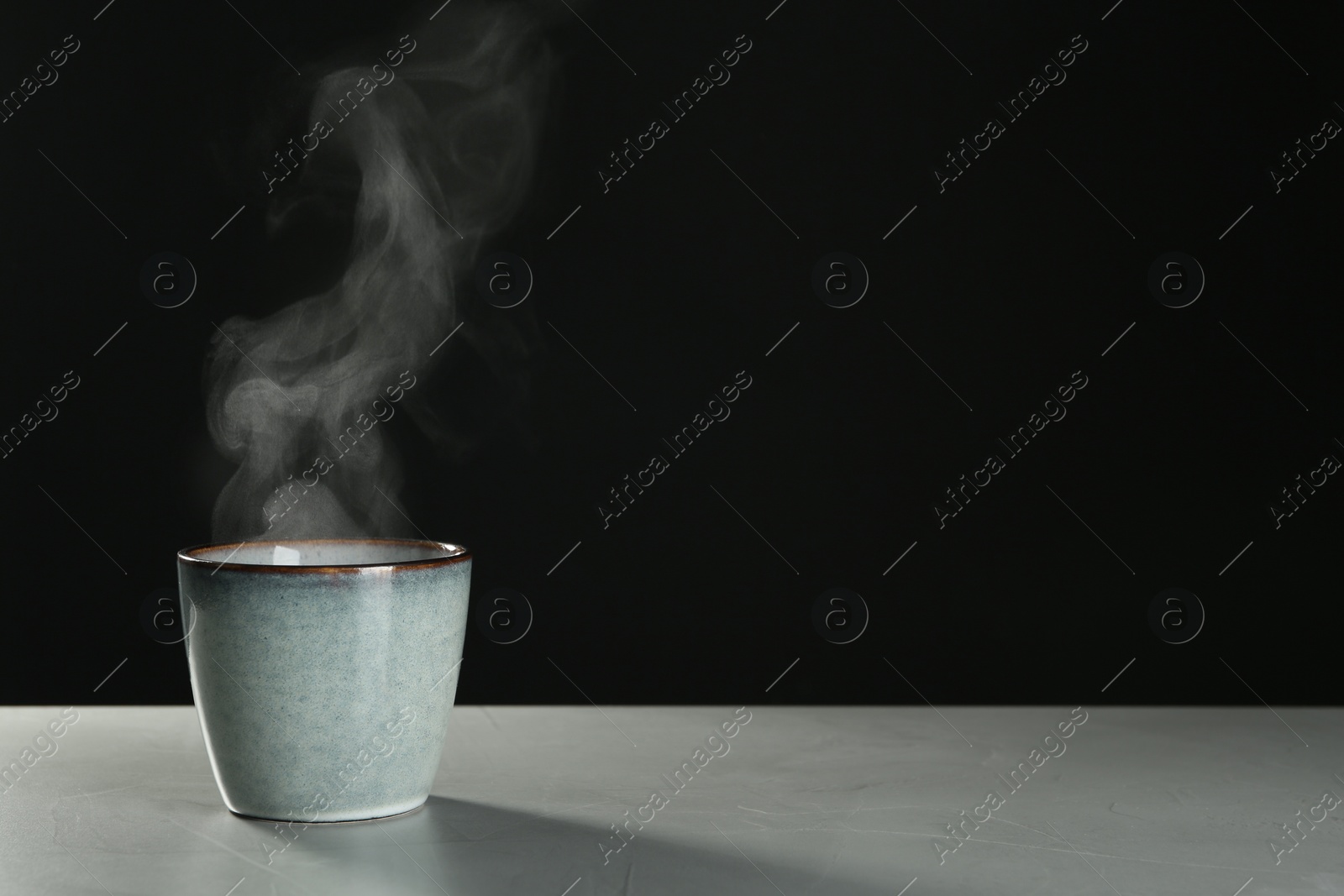Photo of Mug with steam on table against black background. Space for text
