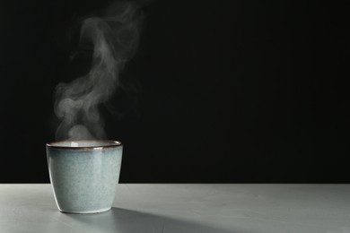 Photo of Mug with steam on table against black background. Space for text