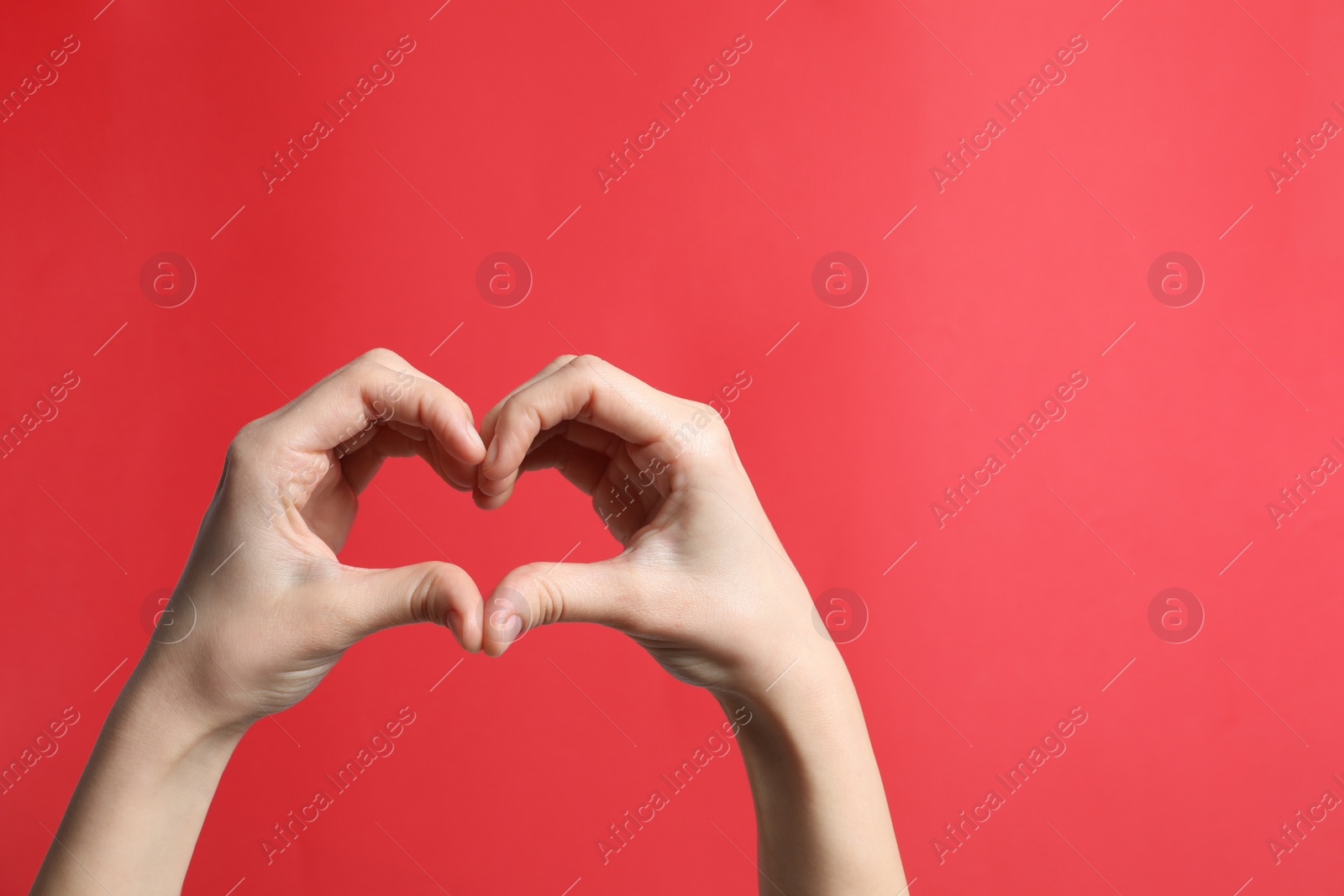Photo of Woman making heart with her hands on red background, closeup. Space for text