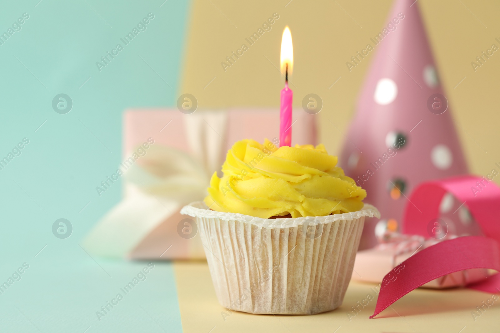 Photo of Tasty birthday cupcake with candle, gift box and party hat on colorful background. Space for text