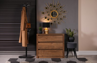 Photo of Wooden chest of drawers with decor, coat stand and mirror in hallway. Interior design