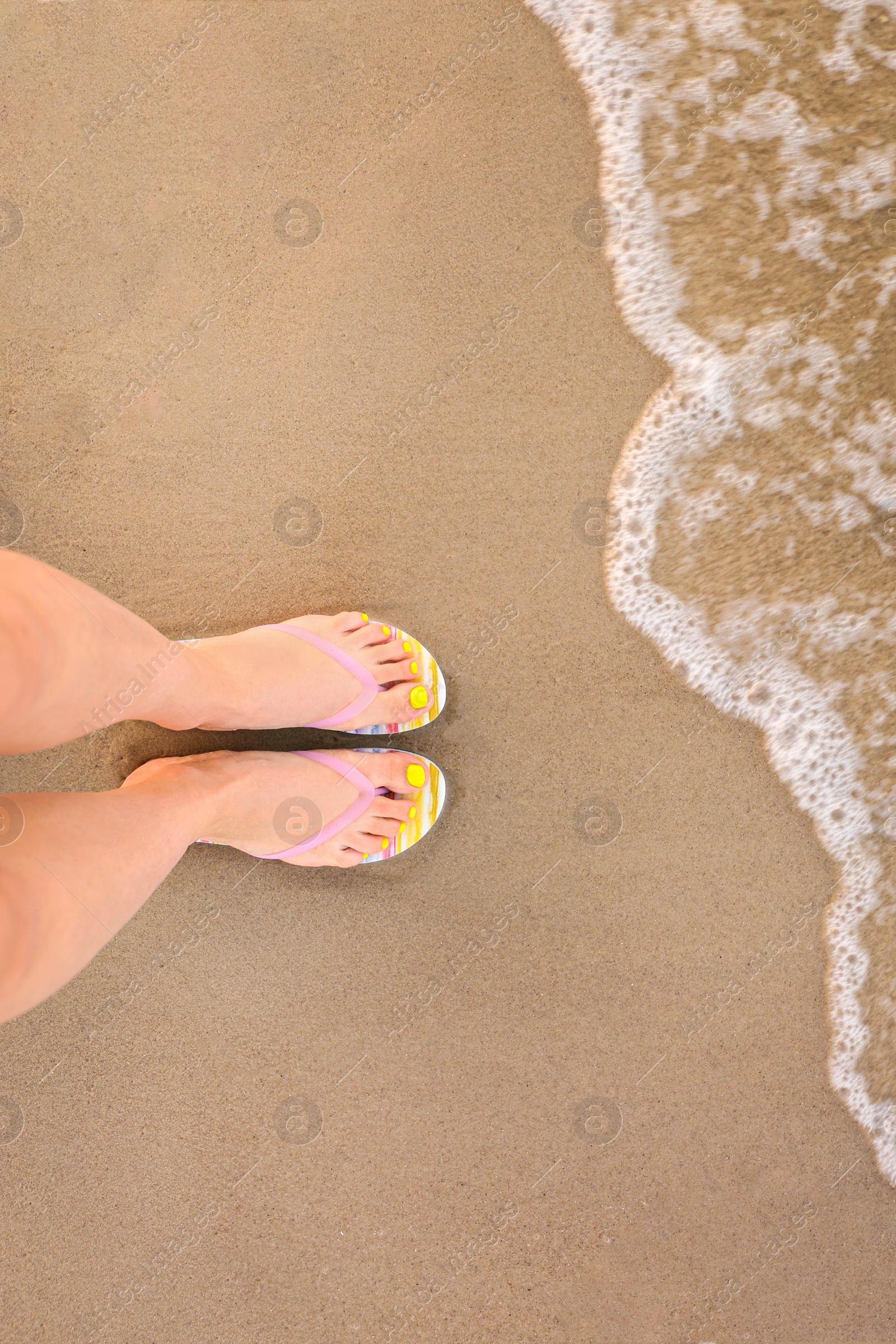 Photo of Top view of woman with stylish flip flops on sand near sea, space for text. Beach accessories